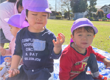 異年齢の園児が一緒に公園でお弁当を食べている。