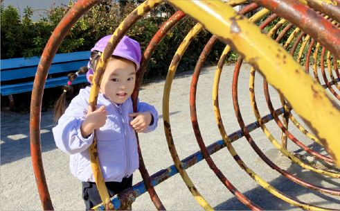 公園のオレンジと黄色の遊具から顔を覗かせて園児。